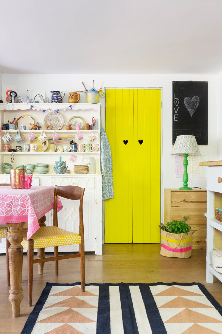 Bright yellow door, geometric print rug and dresser in the colourful kitchen of designer and block print-maker Molly Mahon at her home in Ashdown Forest, East Sussex